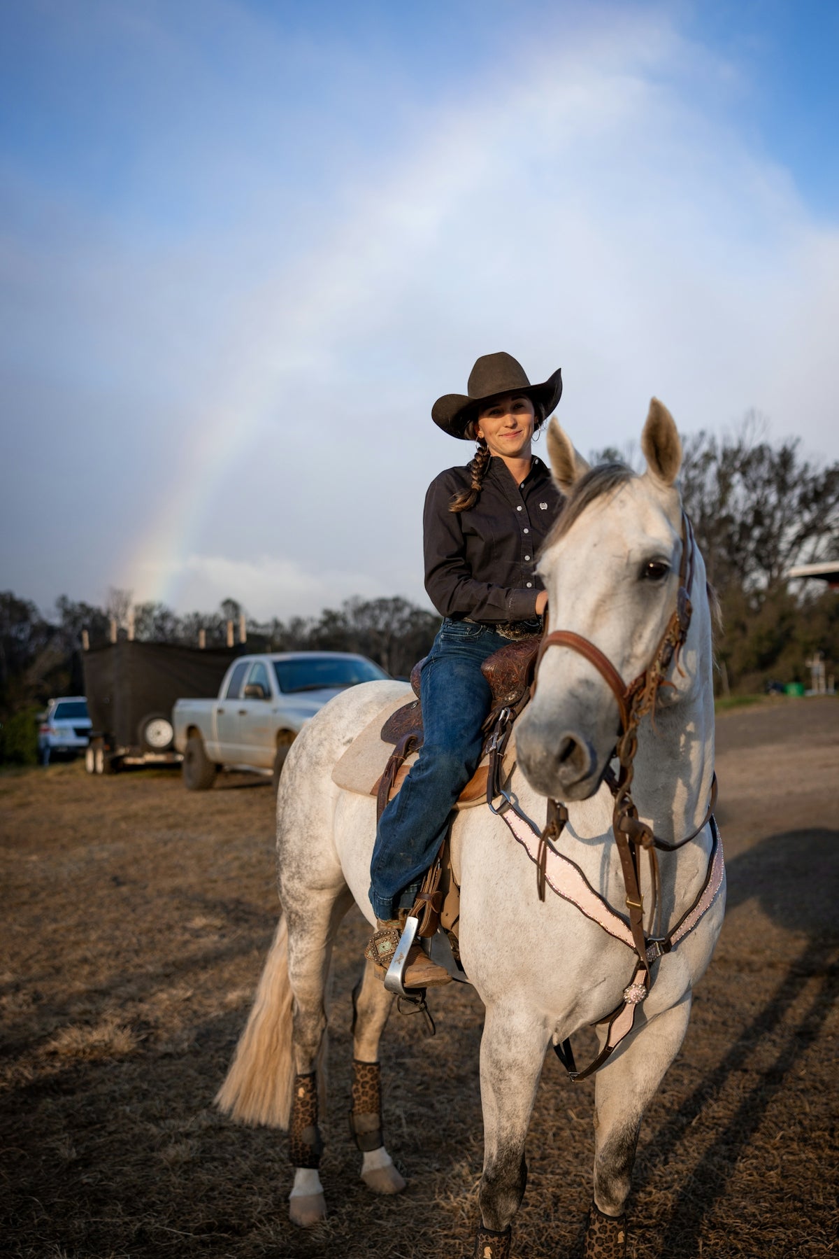 Young woman in cowboy hat riding white horse with rainbow