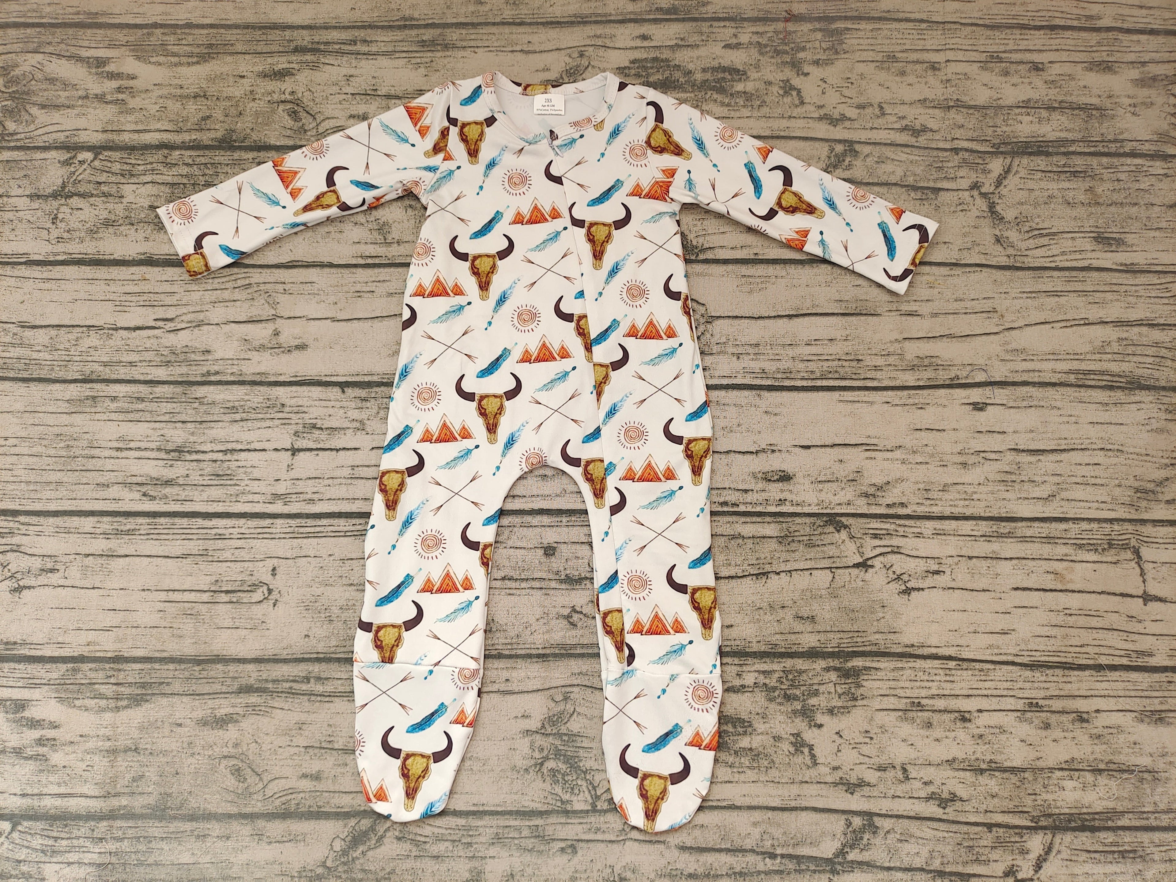 Baby boys' western cow-print footie romper laid flat on a wood backdrop