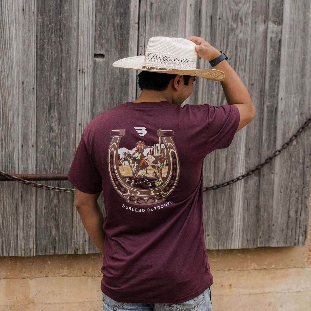 Man wearing BURLEBO Horseshoe Maroon Tee by a barn