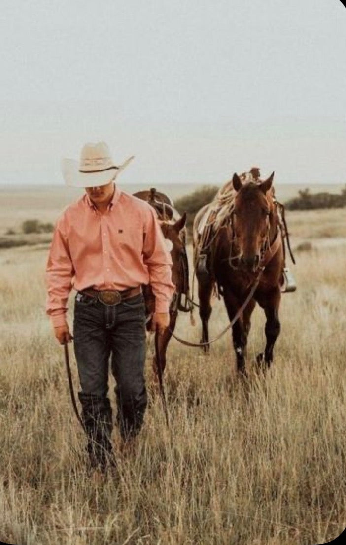 Cowboy walking with horses through ranch grass