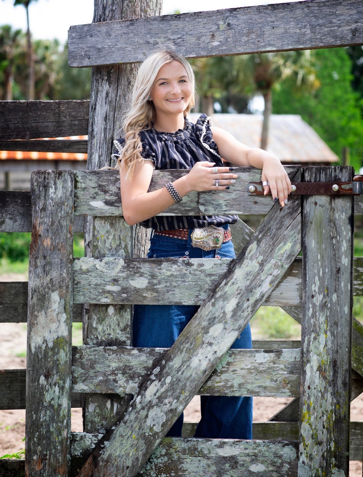 Woman in western wear standing at a weathered ranch gate
