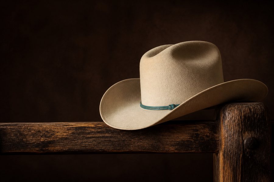 Cream western hat with a turquoise band on a rustic wood rail